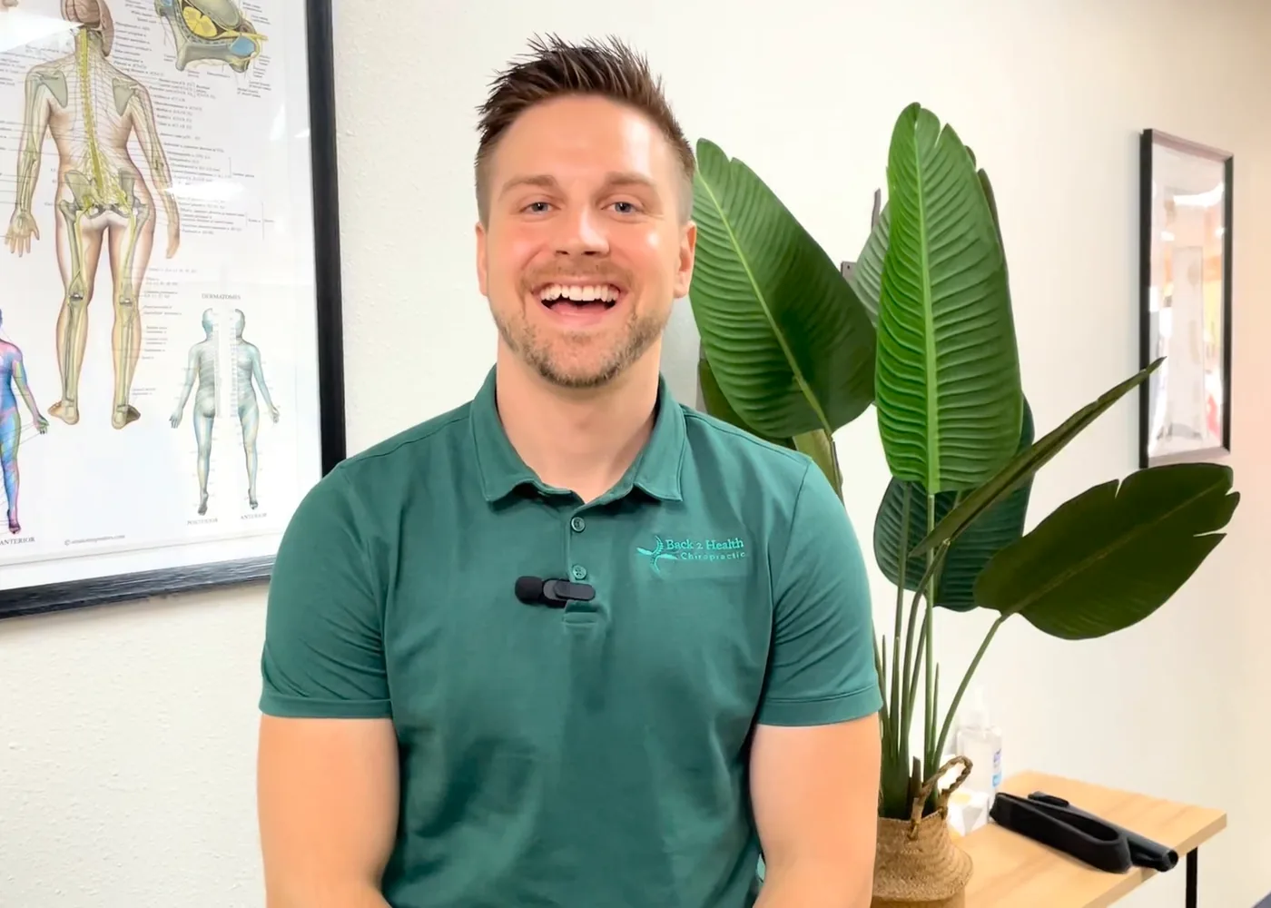 Dr. Brett Chavez smiling in the Back 2 Health Chiropractic office in front of spine anatomy charts