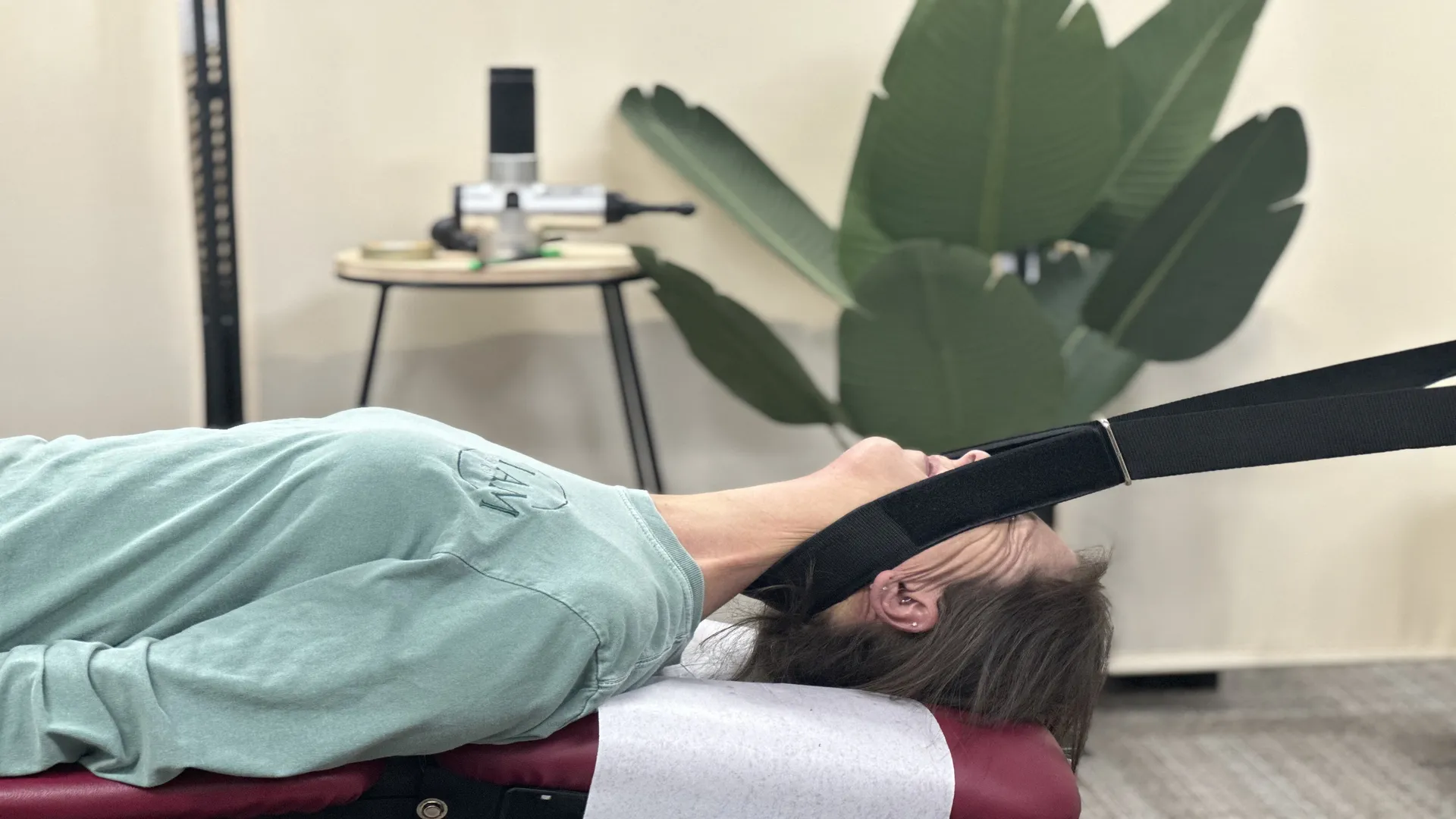 Person lying face up on a treatment table with a cervical traction strap supporting the head, in the clinic treatment room