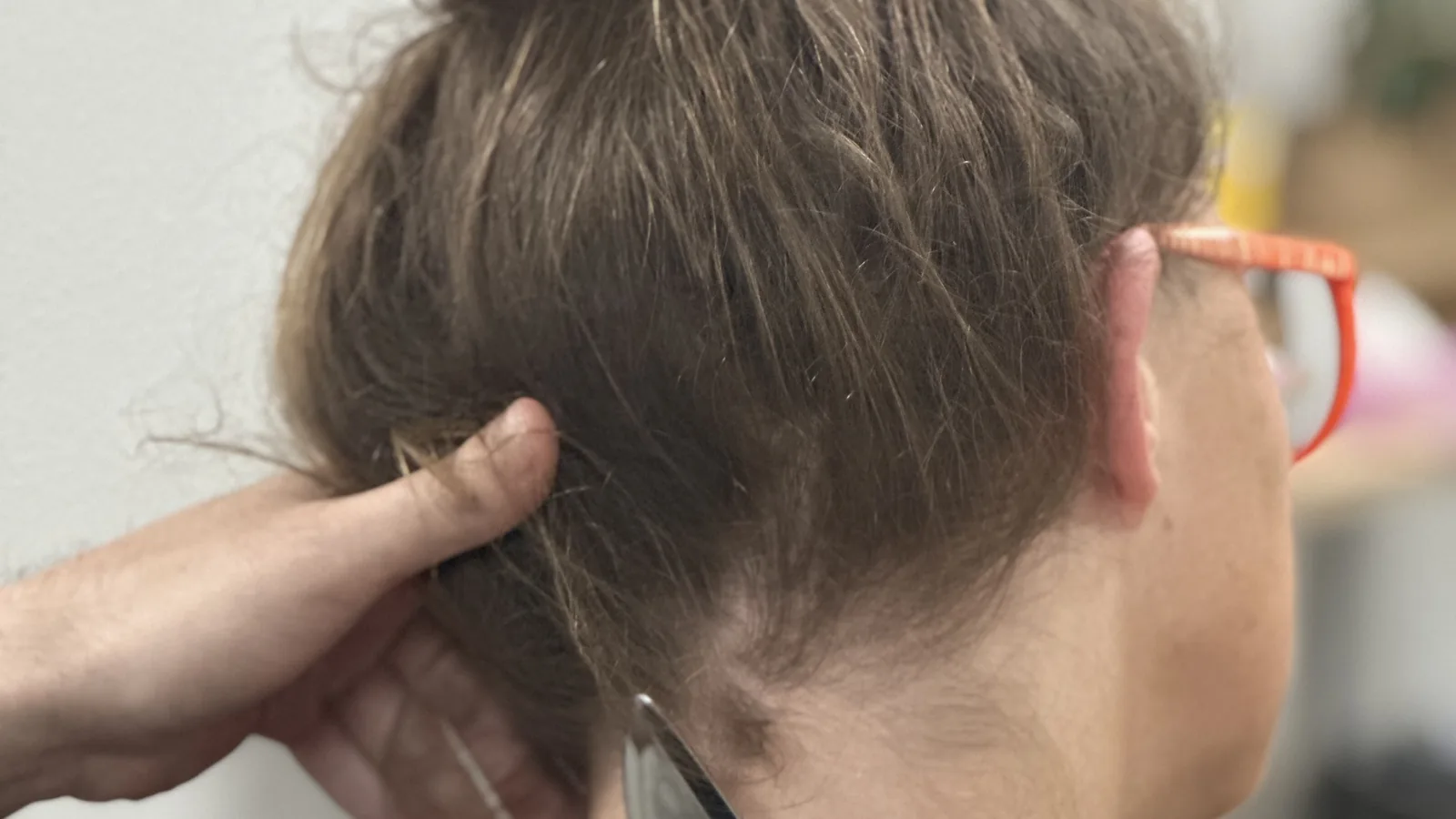 Close-up of the back of a person's head and ear with a provider's hand holding their hair at the base of the skull