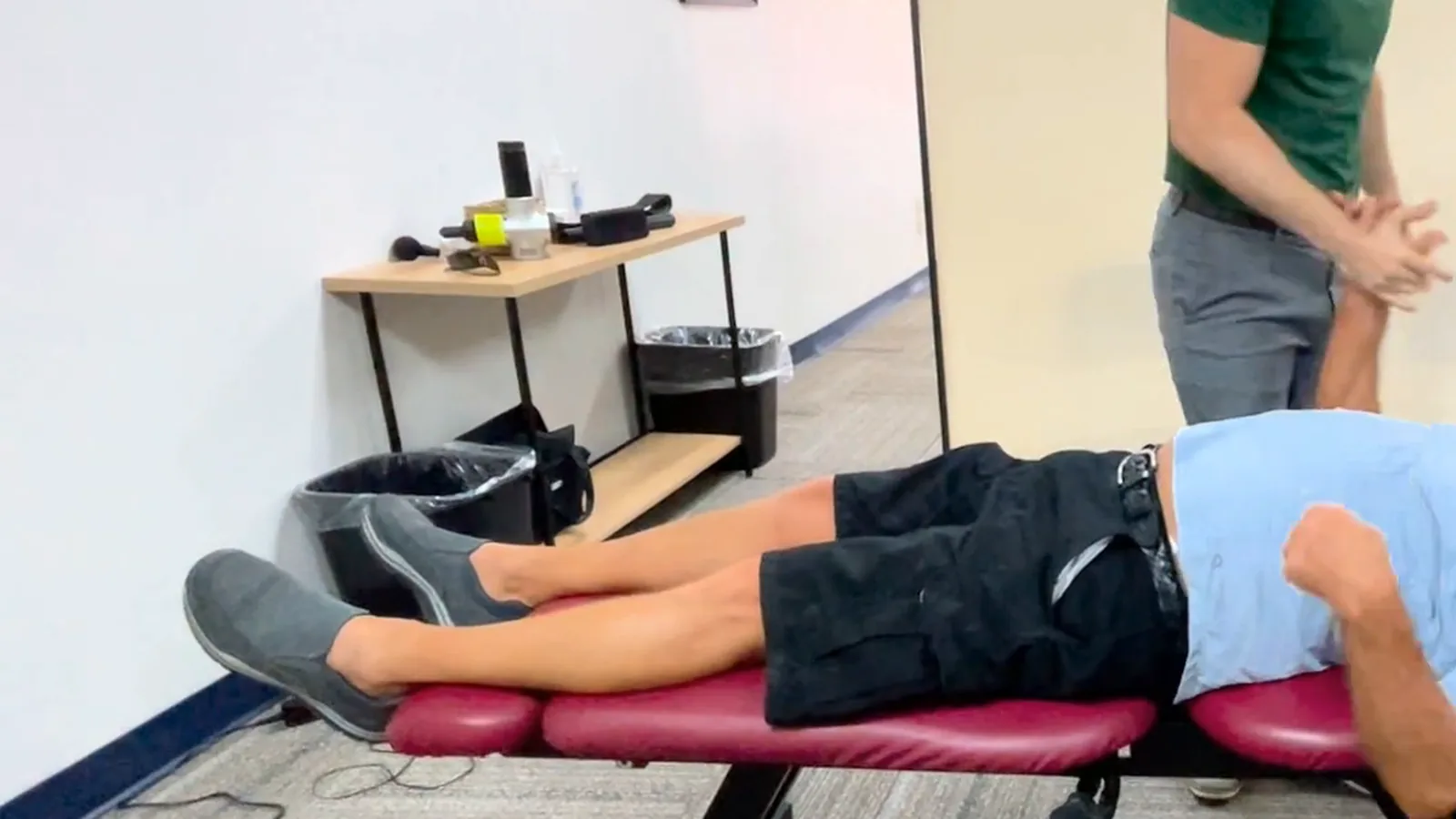 Person lying on a treatment table in the clinic while a provider in a green polo stands beside the table with hands clasped