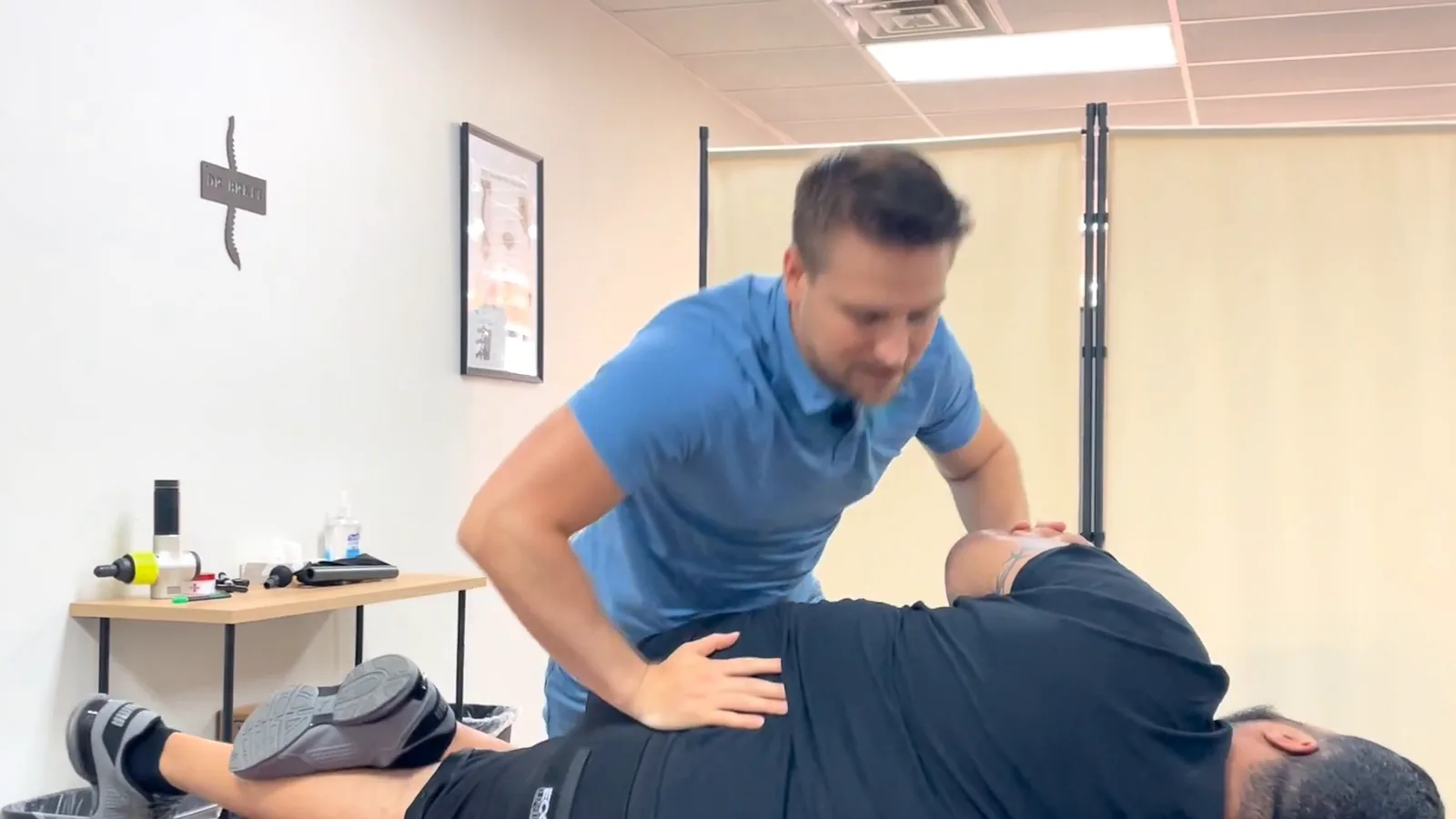 Provider in a blue polo leaning over a patient lying on their side on a treatment table, one hand on the patient's back and the other near the head and neck